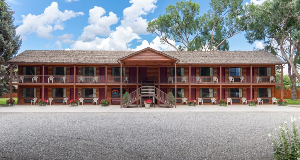 Chuckwagon Lodge in Torrey, UT: a two-story motel with log-style siding, wood-shake roof, covered entrance, upper-floor walkway, and red geraniums along the front, framed by mature trees.