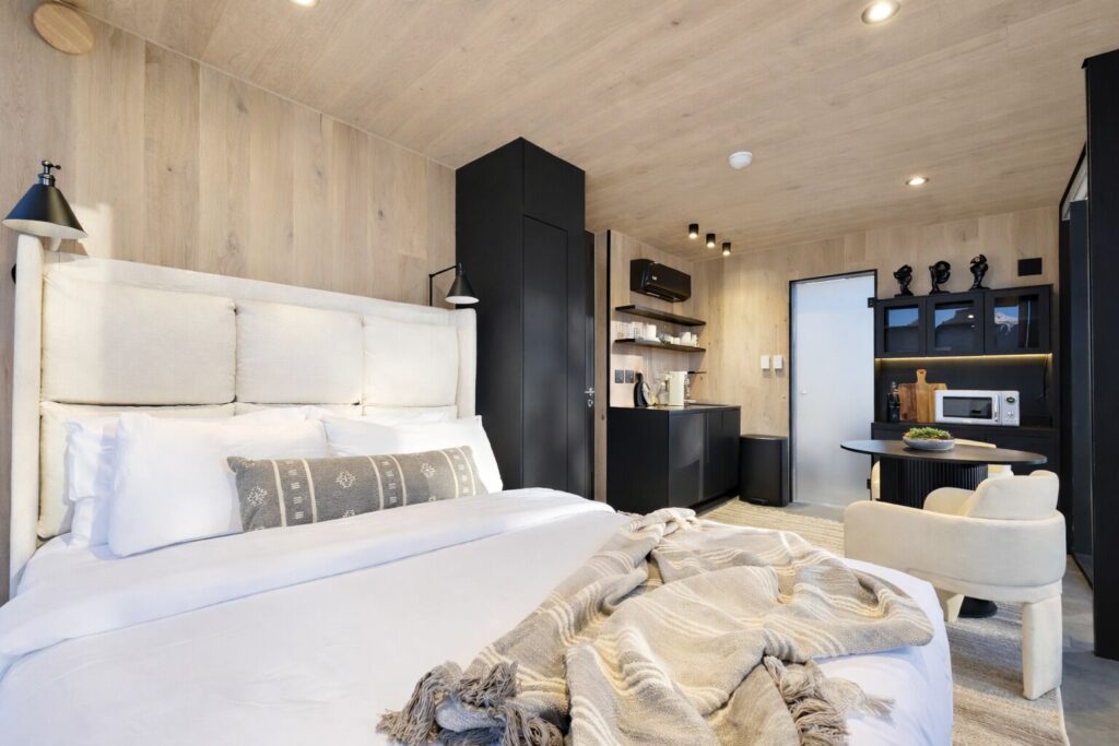Studio guest room at Reflections Resort in Torrey, UT, featuring light wood walls, a king bed with white linens, compact kitchenette with black cabinetry, and a small dining area.