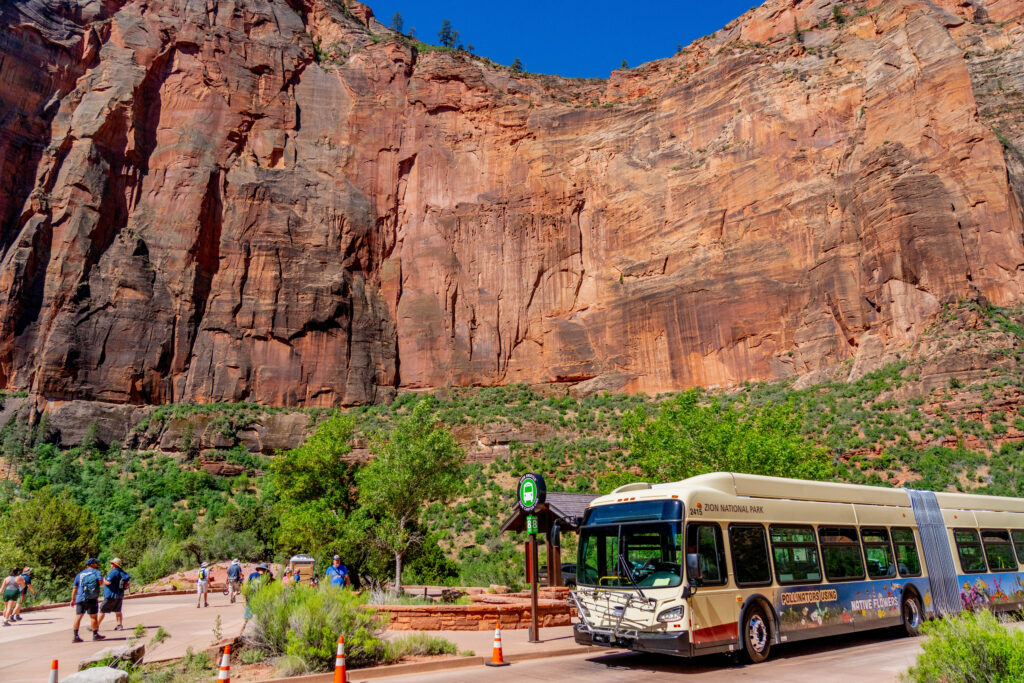 Zion Shuttle paused at Stop 8, Big Bend, with towering red cliffs above.